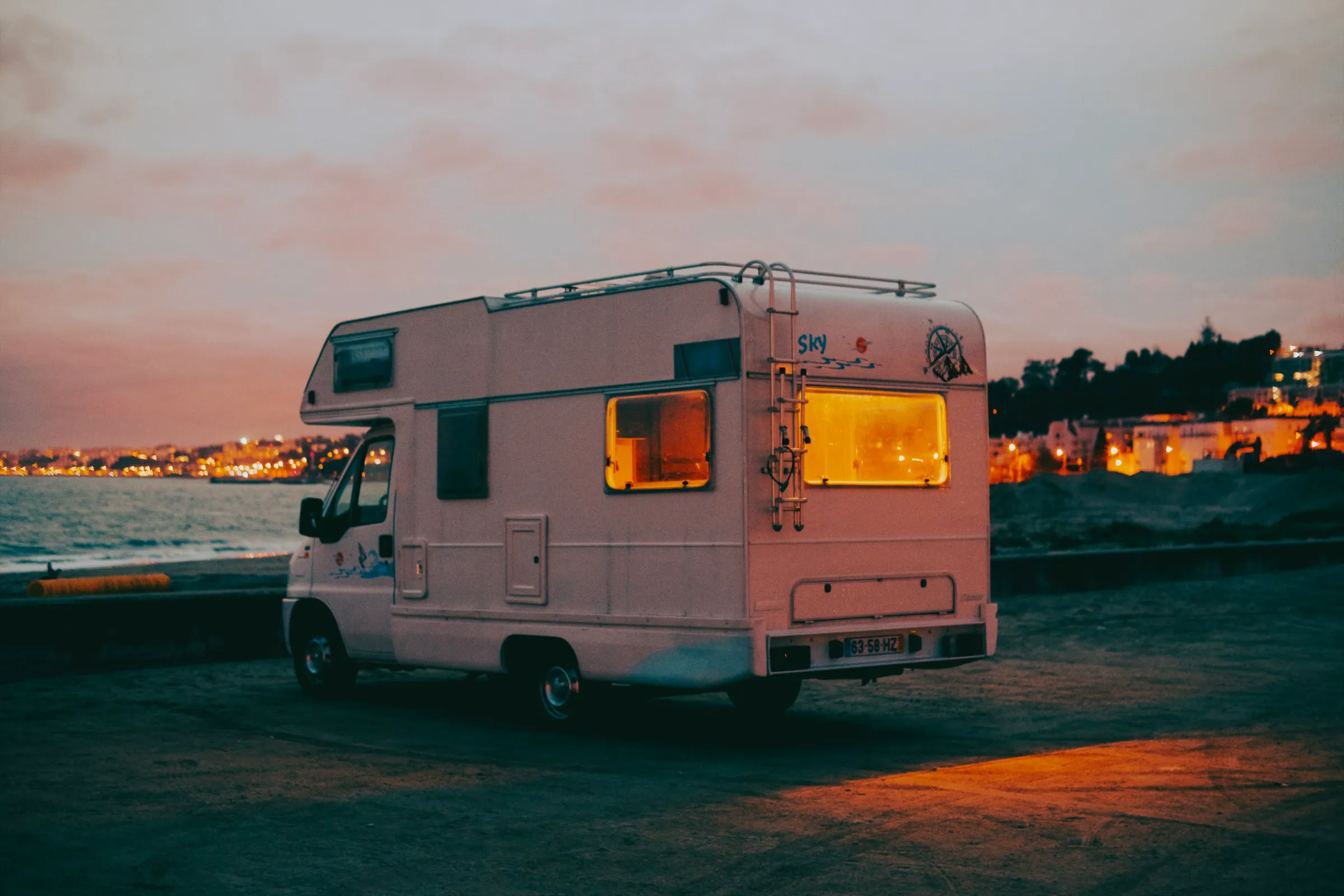 An RV with warmly lit windows parked at dusk