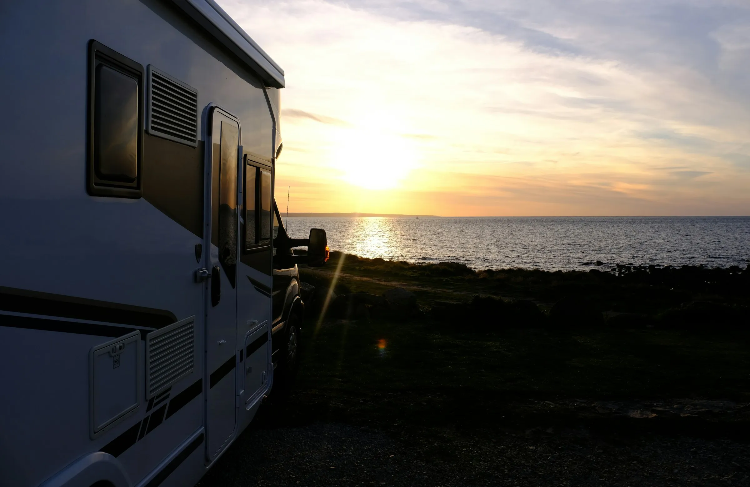 A motorhome parked at the water's edge at golden hour